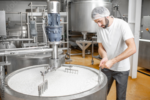 Man mixing milk in the stainless tank during the fermentation process at the cheese manufacturing