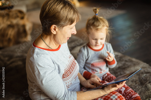 Grandma and granddaughter have fun together reading a book on the bed . Family Christmas concept. Selective focus.