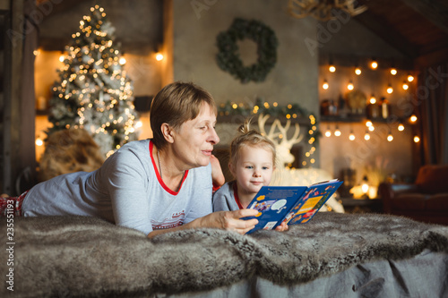 Grandma and granddaughter have fun together reading a book on the bed . Family Christmas concept.