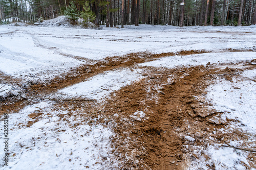 Car Tire Marks on an Empty Field Covered With Snow, Wood in the Background - Cloudy Day