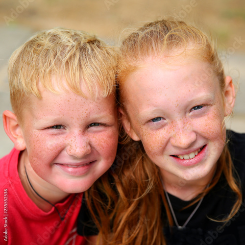 Obraz na płótnie Portrait of two happy pretty redhead girl and boy with blue eyes in sunny day in park