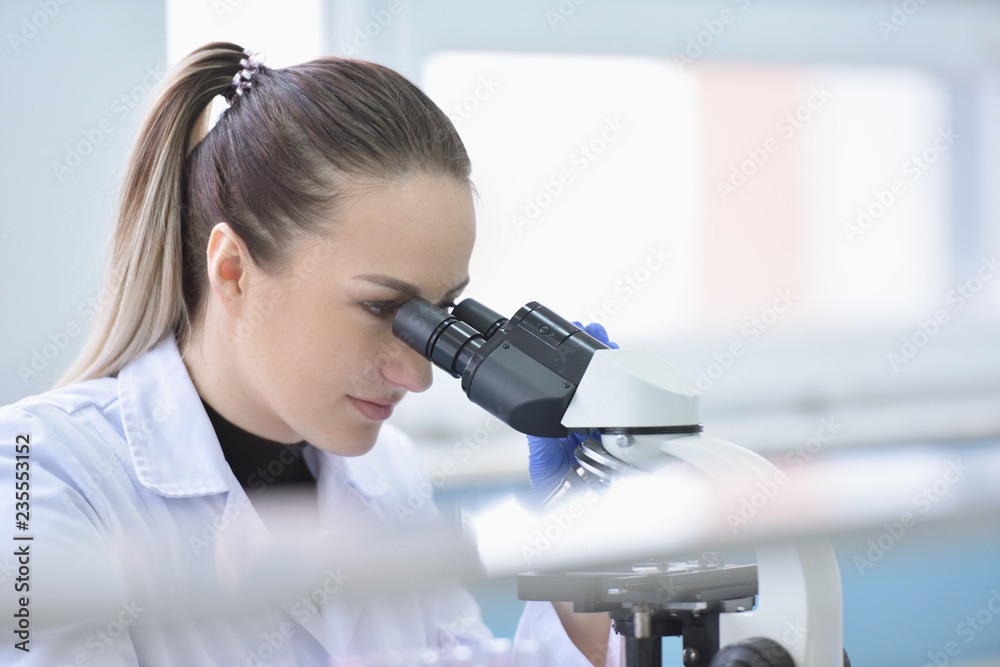 Fototapeta premium Young female male scientist looking through a microscope in a laboratory doing research, microbiological analysis, medicine.