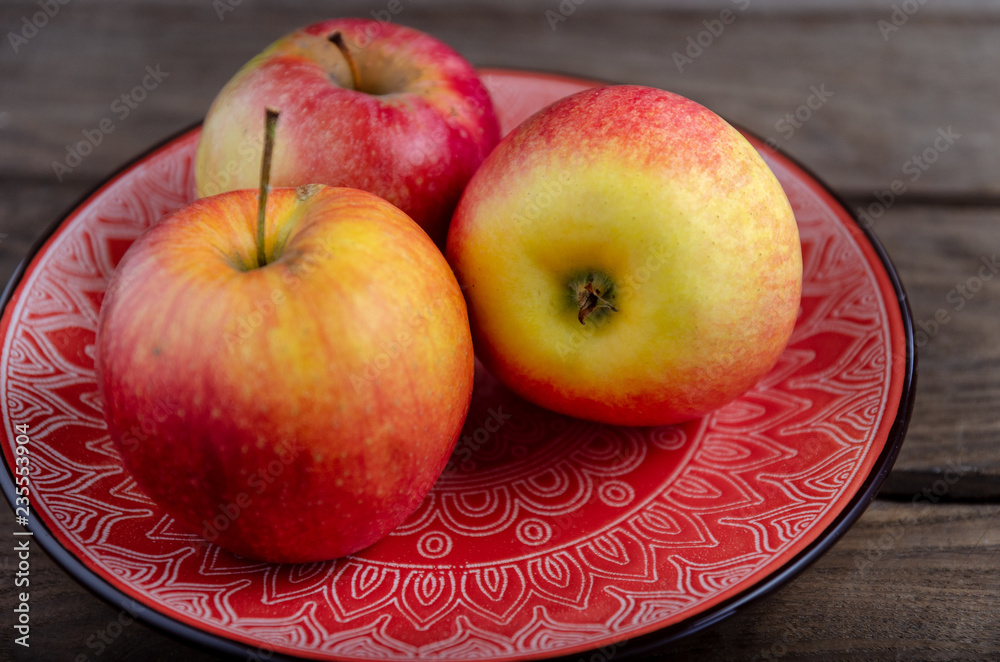 Apples in a ceramic red plate on a wooden table. Apples in a ceramic red plate on a wooden table.