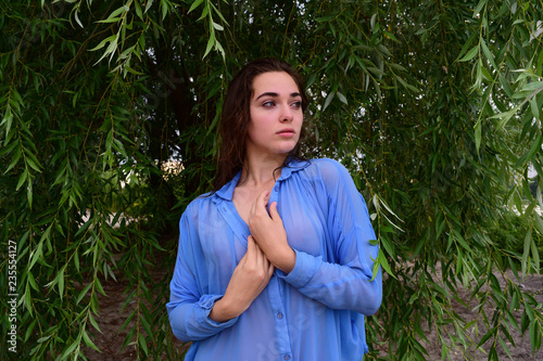 Young wet girl holding hands together in shirt on green background in nature.