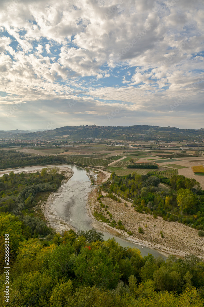 Aerial view of a river with woods, cultivated fields and hills in the background in autumn, Langhe, Piedmont, Italy