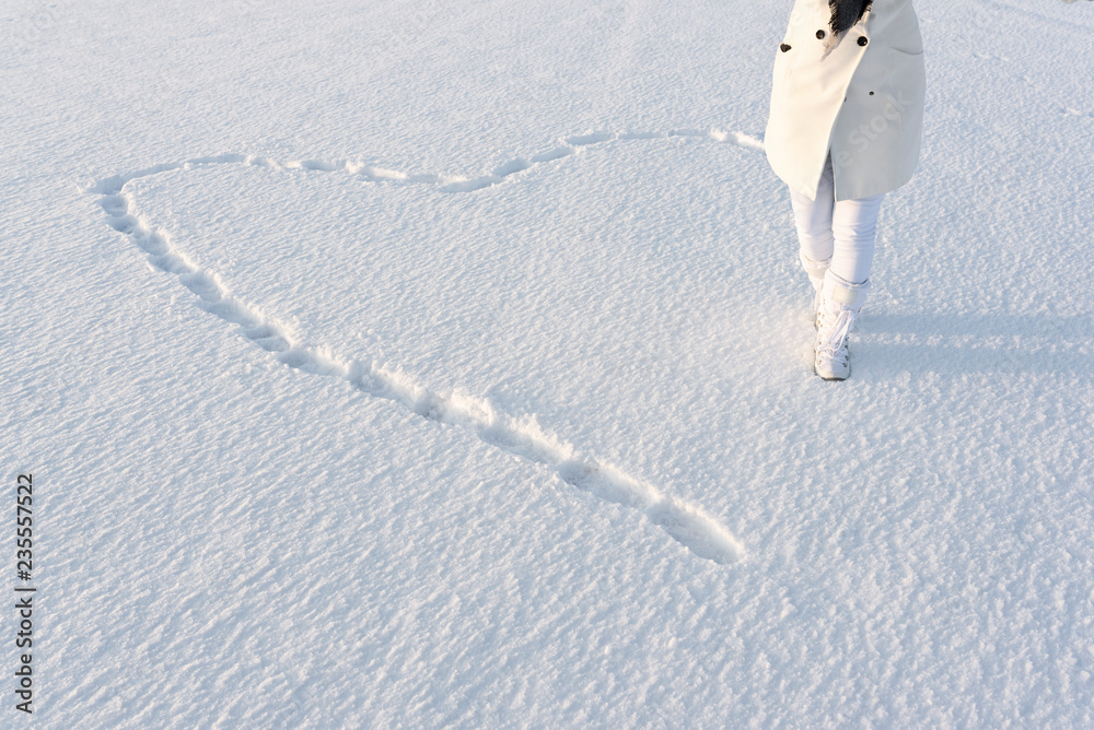 Snow heart made by footsteps. Anonymous woman dressed in white winter coat,  walks on deep snow in snow boots. Stock Photo | Adobe Stock