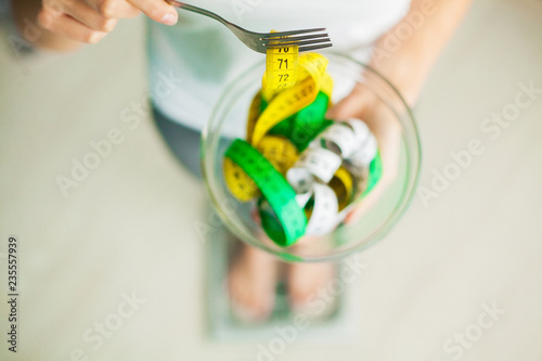 Diet and Weight Loss. Woman holds bowl and fork with measuring tape