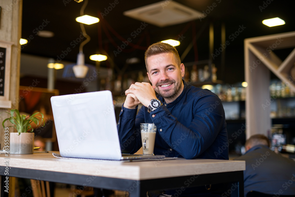 Portrait of smiling man sitting in a cafe bar with his laptop computer. Coffee break.
