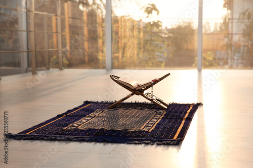 Rehal with open Quran and Muslim prayer beads on rug indoors