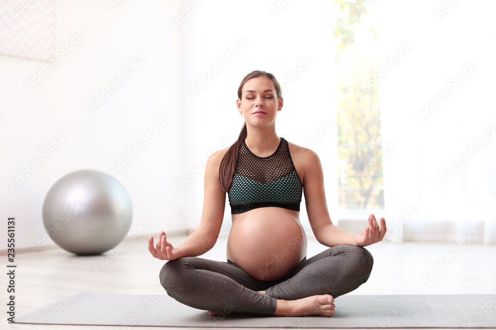 Young pregnant woman in fitness clothes meditating at home