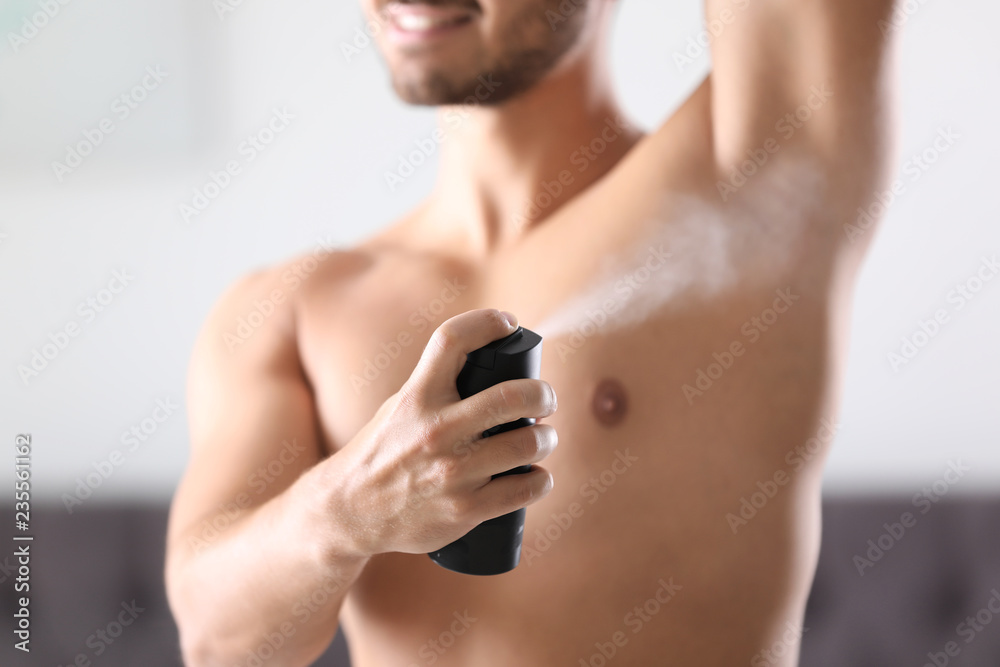 Fototapeta premium Handsome young man applying deodorant in room