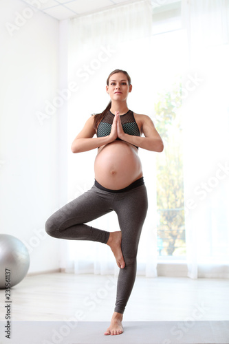 Young pregnant woman in fitness clothes practicing yoga at home