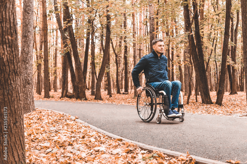 Fototapeta premium A young man in a wheelchair rides along the park road.