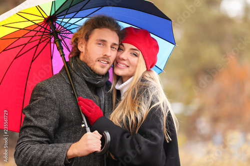 Young romantic couple with umbrella outdoors on autumn day