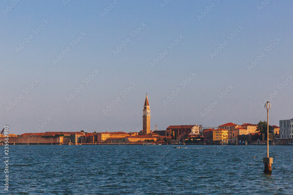 Bell tower over Venetian houses by water at sunset, in Venice, Italy