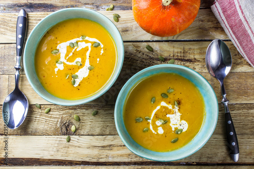 Roasted pumpkin and carrot soup with cream and pumpkin seeds on wooden background. Top view. Copy space