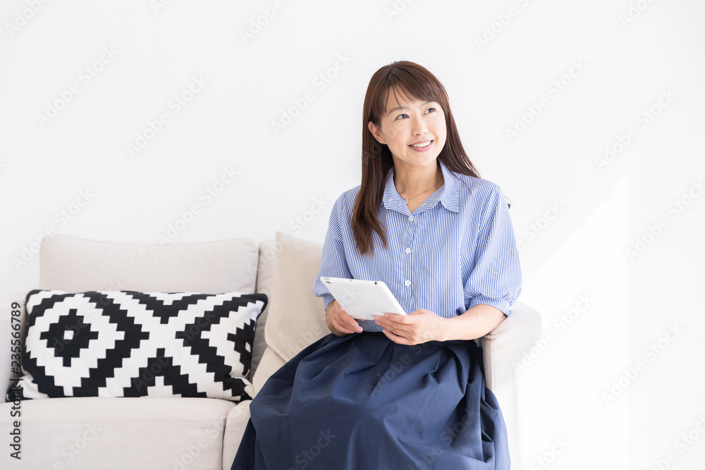 部屋でタブレットを見るミドル女性