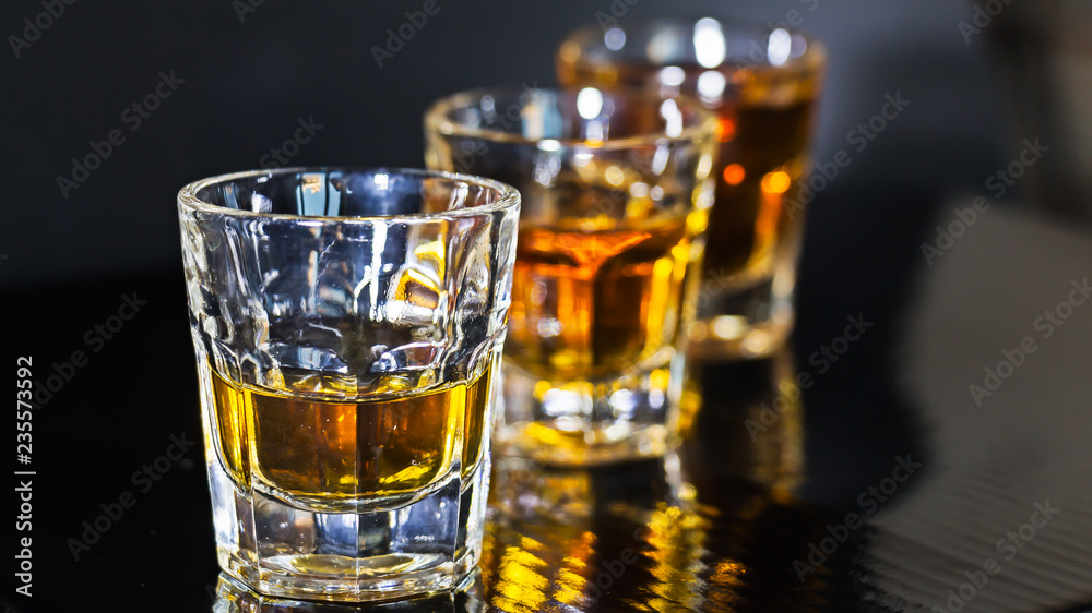 Shots de whisky en fila sobre fondo negro y luz directa en ellos