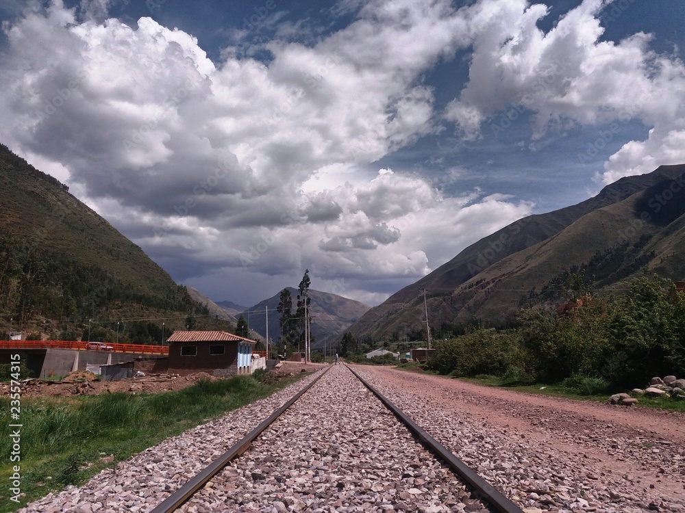 Train tracks close to grass and houses, distant mountains, cloudy sky background, location quispicanchi, cusco, peru. Train tracks close to grass and houses, distant mountains, cloudy sky background, location quispicanchi, cusco, peru.