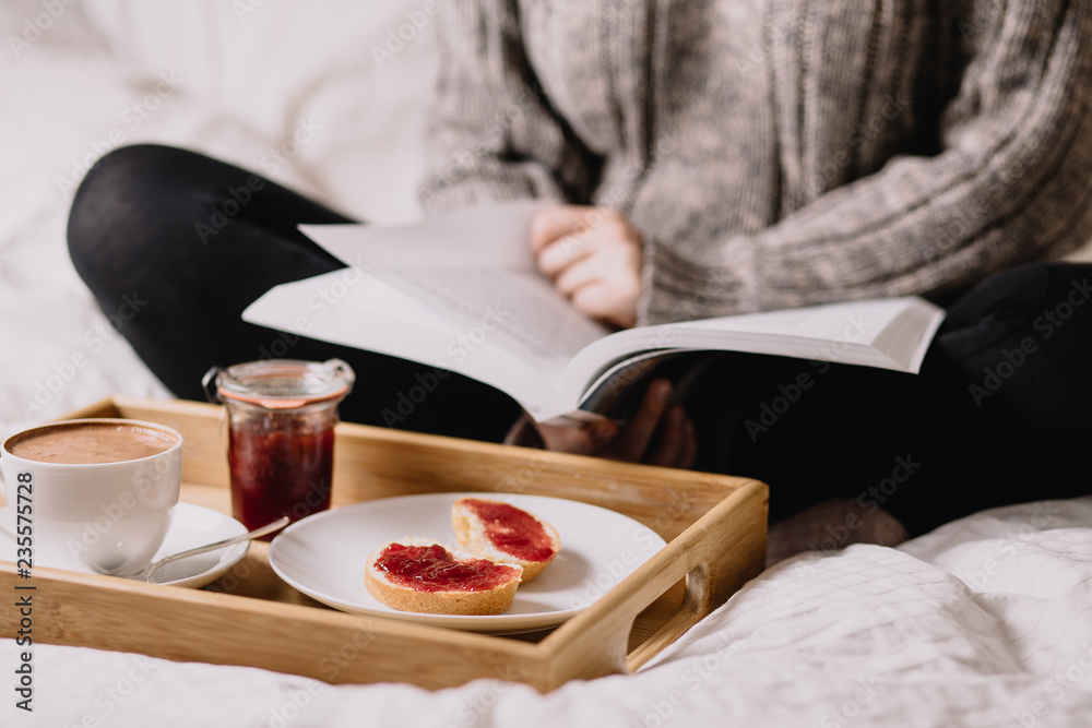 Woman on a bed, reading a book and drinking coffee