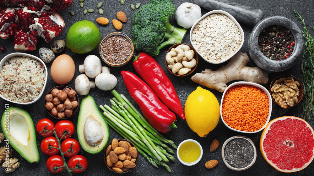 Healthy food clean eating selection: fruit, vegetable, seeds, superfood, cereal, leaf vegetable on black concrete background. Flat lay