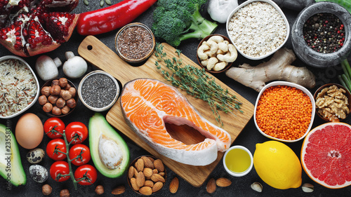 Healthy food clean eating selection: fish, fruit, nuts, vegetable, seeds, superfood, cereals, leaf vegetable on black concrete background. Flat lay