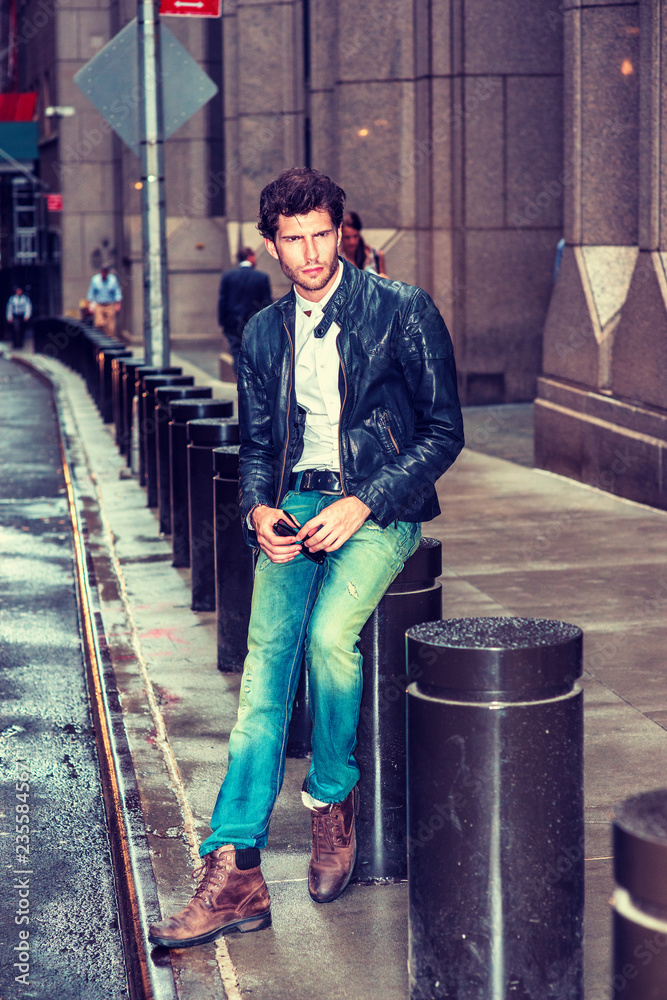 Man Casual Fashion. Dressing in black leather jacket, blue jeans, brown  boot shoes, holding sunglasses, an European Businessman with beard sitting  on street in New York after raining, sad, thinking. Stock Photo