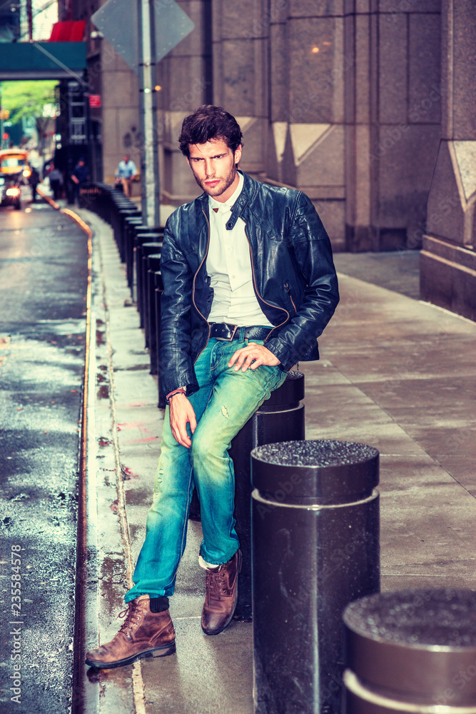 Man Casual Fashion. Dressing in black leather jacket, blue jeans, brown  boot shoes, holding sunglasses, European Businessman with beard sitting on  street in New York after raining, sad, thinking. Stock Photo