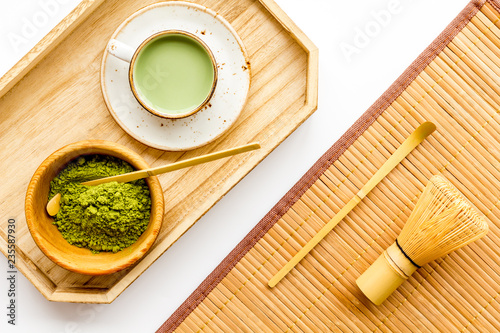 Coffee and cocktails with matcha concept. Matcha latte near bowl with matcha powder and whisk on wooden tray white background top view photo