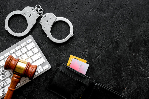 Arrest for stealing money online concept. Handcuff near keyboard, judge gavel and bank card on black background top view copy space