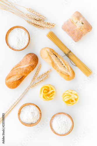 Products made of wheat flour. White flour in bowl, wheat ears, fresh bread and raw pasta on white background top view