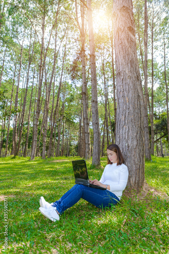 Portrait of pretty young woman sitting on green grass in park summer day while using laptop