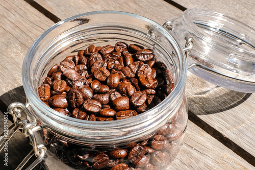 Close up dark brown roasted coffee beans in a glass jar in daylight 