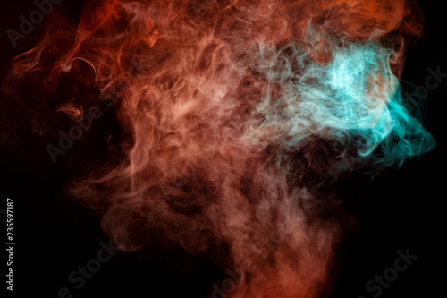 A background of blue, red and green wavy smoke in the shape of a ghost's head or a man of mystical appearance on a black isolated ground. Bright abstract pattern of steam from vape.