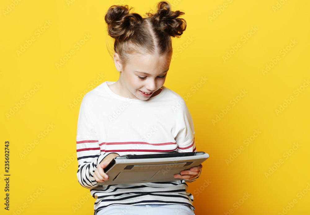 Little girl with tablet on yellow studio background. Little girl with tablet on yellow studio background.