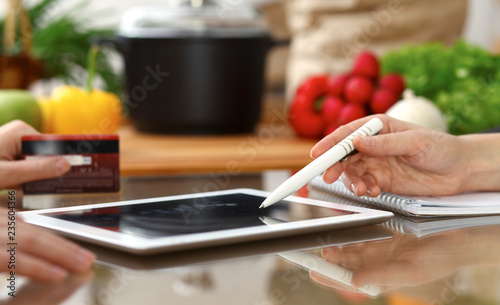 Close-up of human hands using tablet or touch pad. Two women in kitchen. Cooking, friendship or online shopping concepts