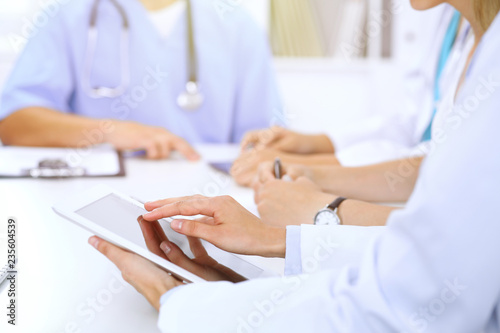 Doctor using tablet computer at medical meeting, closeup. Group of colleagues at the background photo