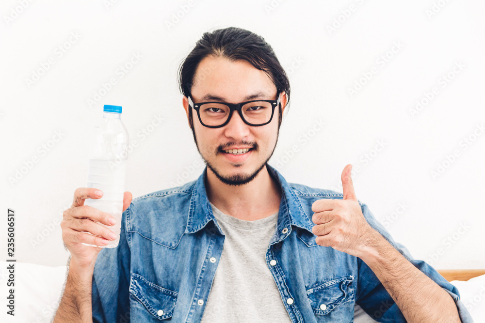 Healthy young man drinking water from a bottle while relaxing and feeling fresh at home Healthy young man drinking water from a bottle while relaxing and feeling fresh at home