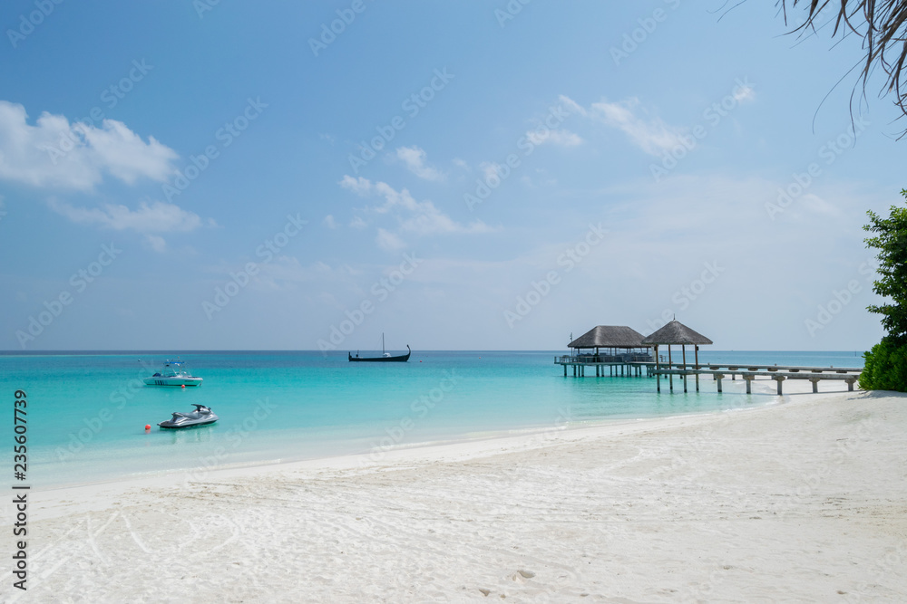 white sand beach, wooden jetty, jet ski, motorboat and sailboat on turquoise lagoon in Maldives