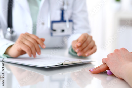 Doctor and patient talking while sitting at the desk in hospital office  close-up of human hands. Medicine and health care concept