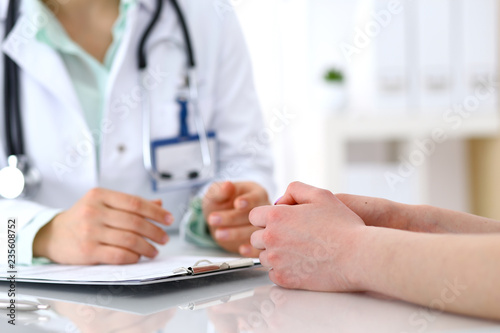 Doctor and patient talking while sitting at the desk in hospital office, close-up of human hands. Medicine and health care concept