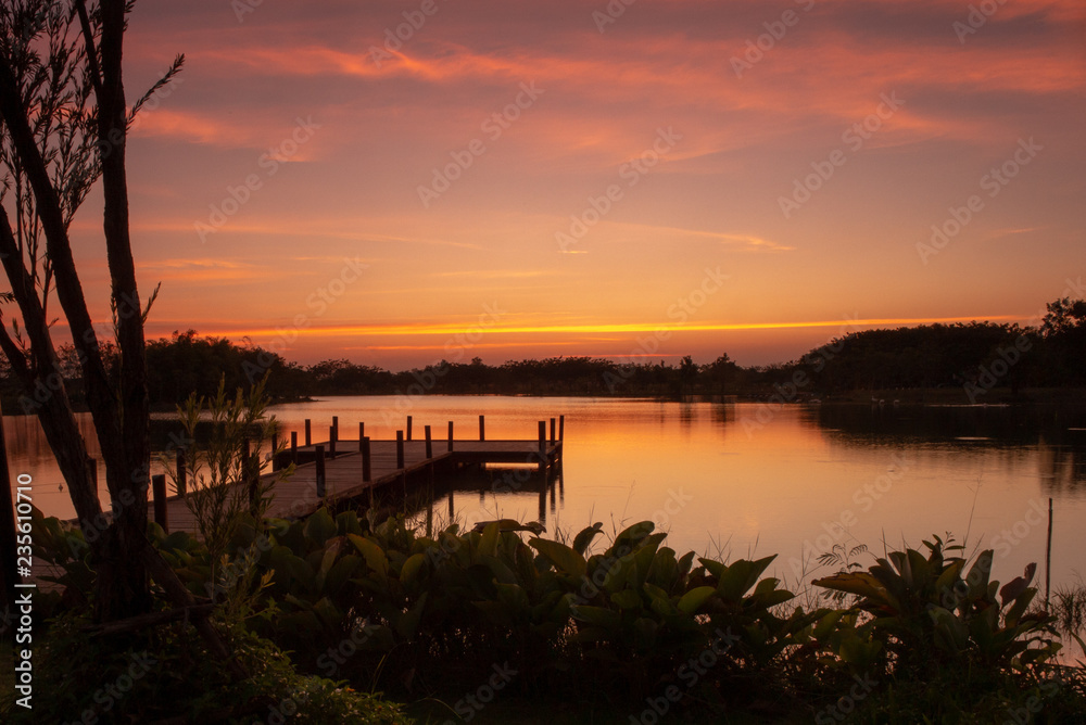 Wooden walkway into the lake with natural scenery of sunset and silhouette of forest in background