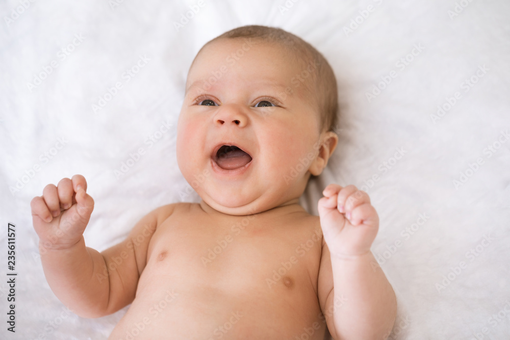 Portrait of cute adorable baby boy lying down and smiling first time on white bed background. Newborn baby smiling and feel happy at home Portrait of cute adorable baby boy lying down and smiling first time on white bed background. Newborn baby smiling and feel happy at home