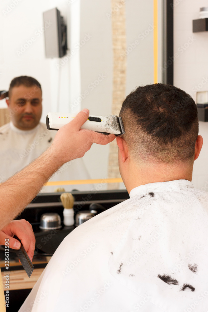 Fototapeta premium Back view of man getting short hair trimming at barber shop with clipper machine