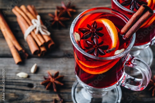 Mulled red wine with spices and orange in glass on a wooden rustic background.