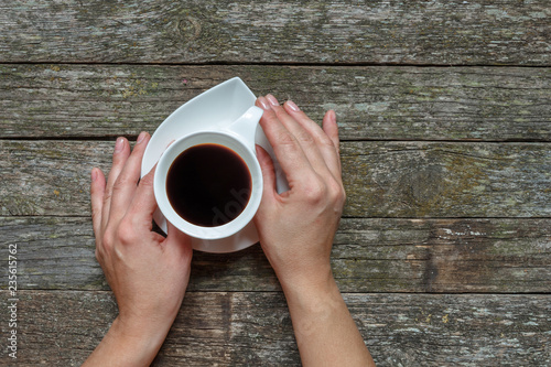 Female hands holding a cup of coffee on a wooden stree, flat lay top view