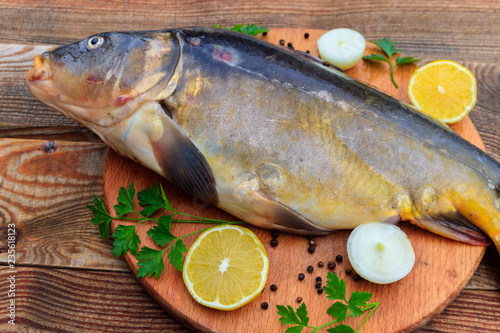 Fototapeta Naklejka Na Ścianę i Meble -  Raw carp fish with lemon, onion, pepper and parsley on cutting board on rustic wooden table