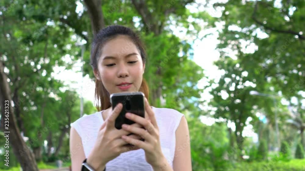 Young beautiful chinese woman holding smart phone and listen song while walking cardio exercise and running in the morning. Healthcare of heart, cardiovascular and mental. Concept of relax and technol Young beautiful chinese woman holding smart phone and listen song while walking cardio exercise and running in the morning. Healthcare of heart, cardiovascular and mental. Concept of relax and technol