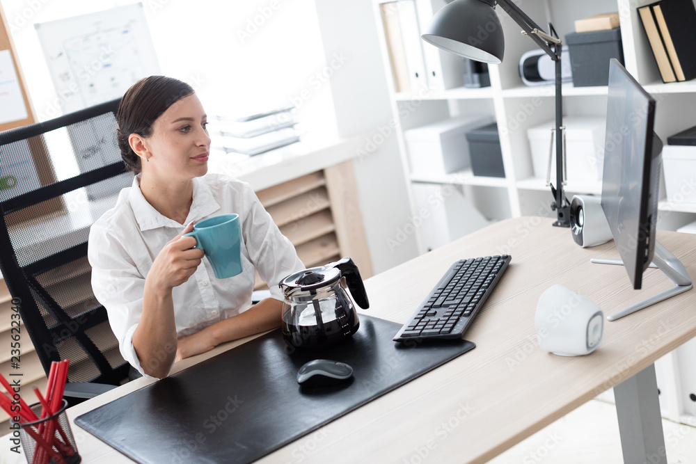 Fototapeta premium A young girl sitting at a table in the office and holding a Cup.