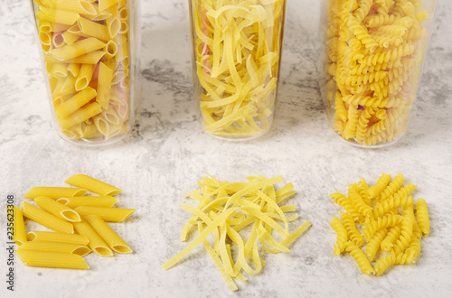 Different types of raw pasta in containers on a light background. Fettuccine, fusilli, penne. Storage products at home